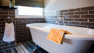 A bathroom with a freestanding bathtub, a towel rack with a white towel, and a window with a view of the outside.