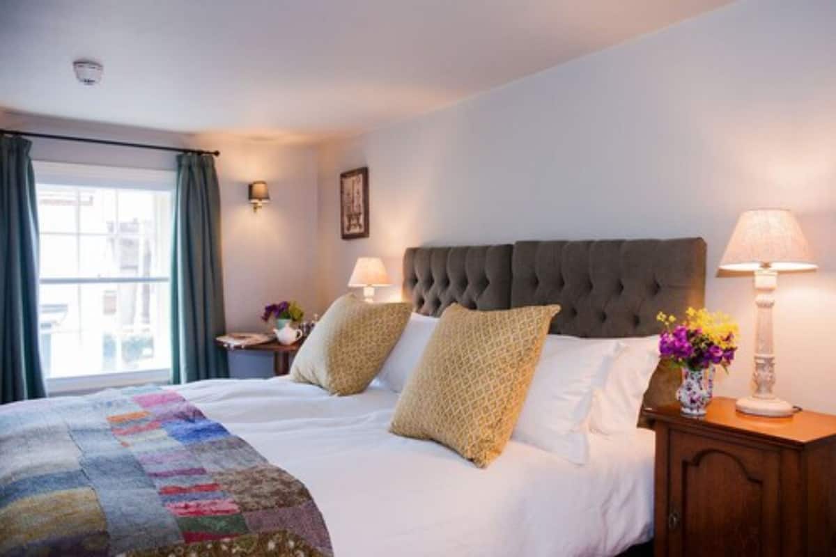 A hotel room with a large bed, two bedside lamps, a nightstand, a window with curtains, and a wall-mounted picture.