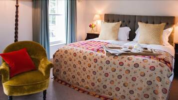A hotel room with a large bed, a yellow armchair with a red pillow, and a window with curtains.