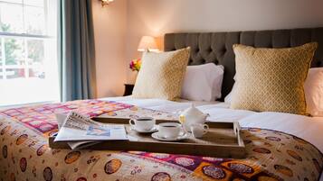 A neatly made bed with a tray of breakfast items, including two cups of coffee and a teapot, on a colorful quilt.