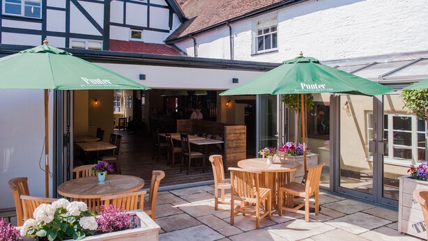 An outdoor patio area with wooden tables and chairs, green umbrellas, and potted plants.