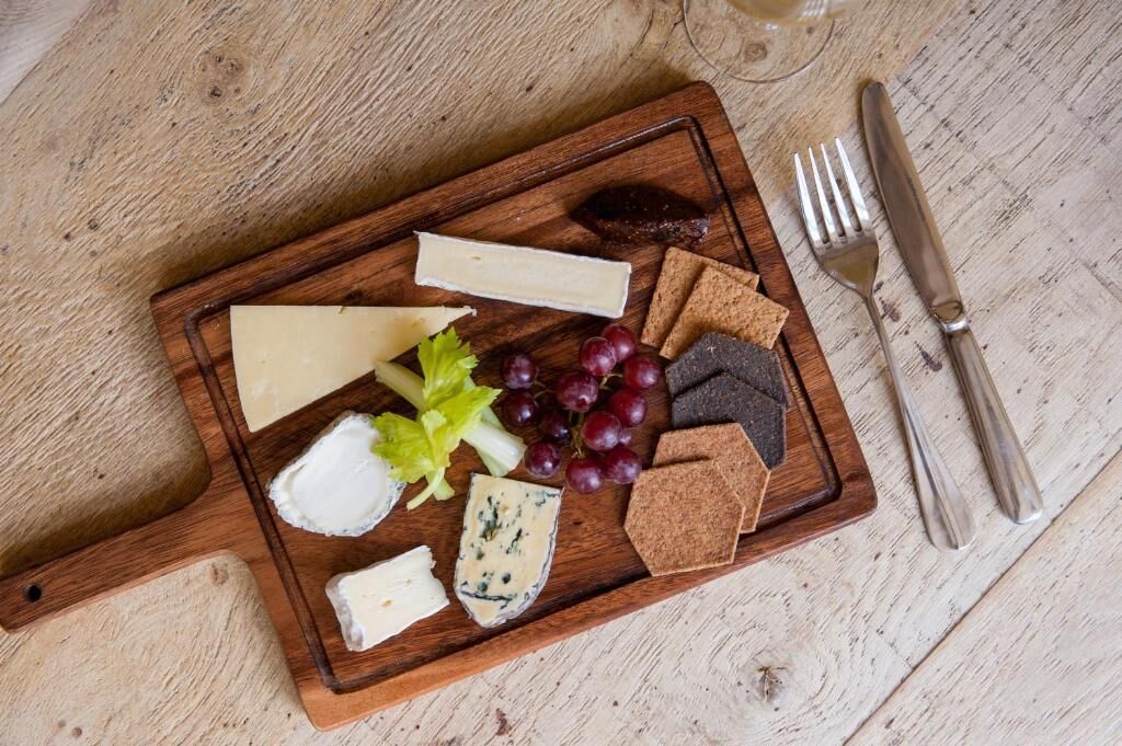 Una tabla de madera con varios quesos, uvas y galletas.