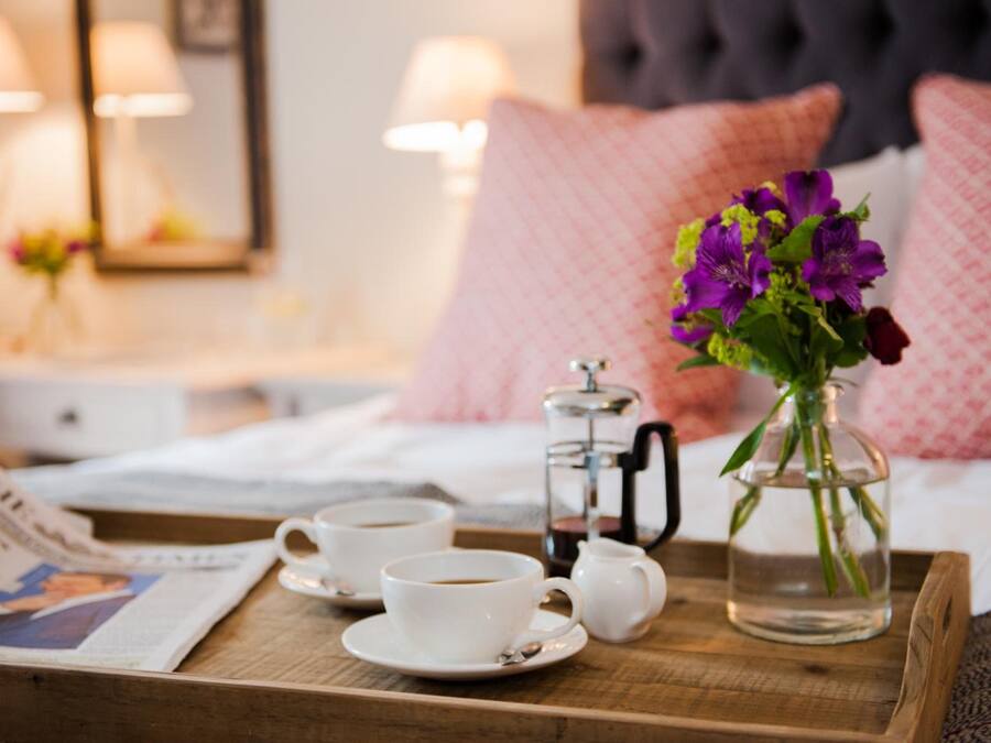 A breakfast tray with two cups of coffee, a teapot, and a vase of flowers on a wooden tray.