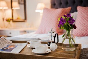 Un plateau de petit-déjeuner avec deux tasses de café, une théière et un vase de fleurs, le tout posé sur un plateau en bois.