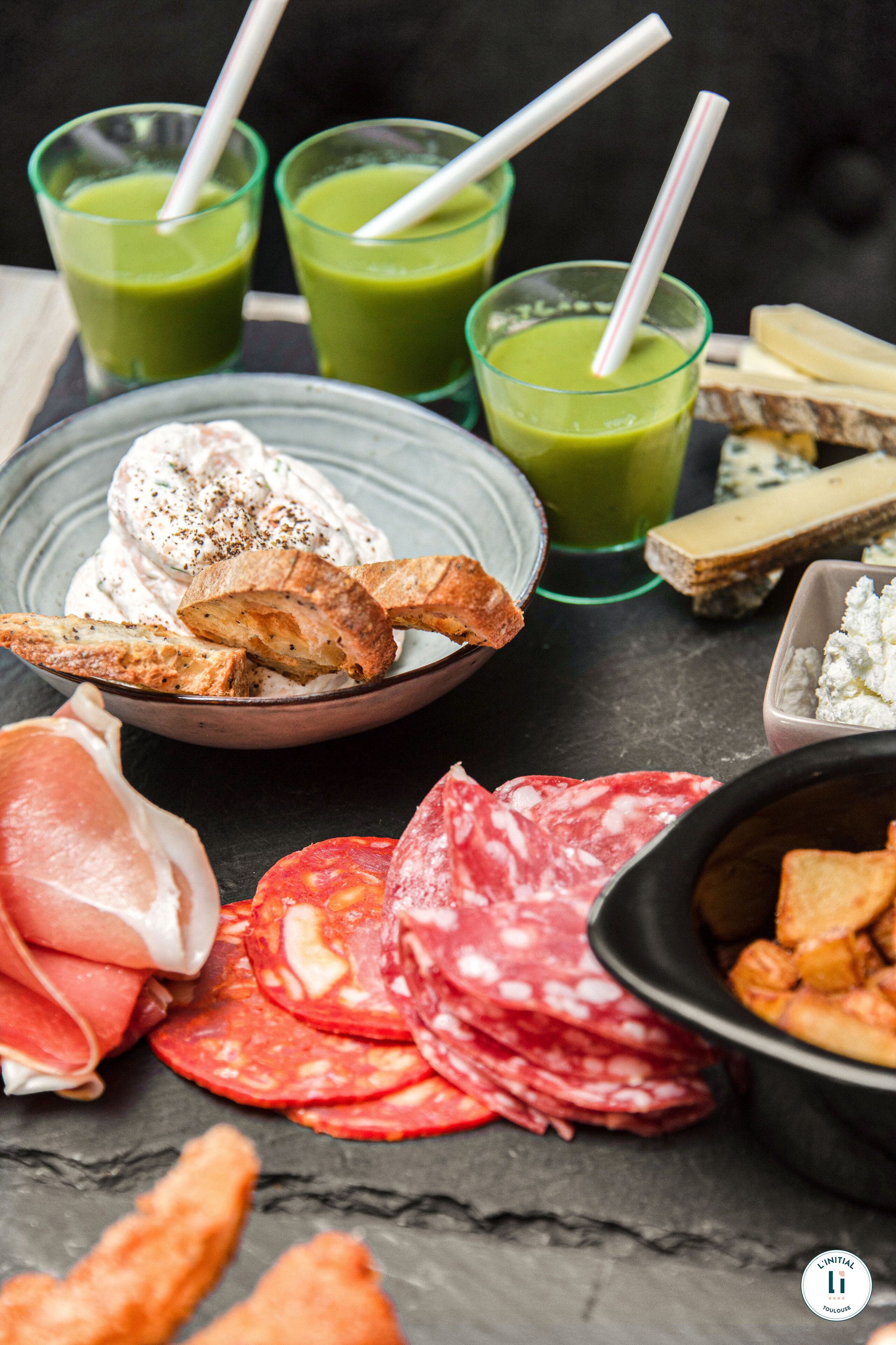 A variety of food items including green smoothies, cheese, cured meats, and bread.