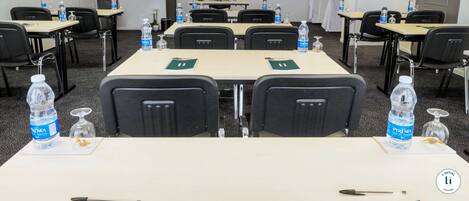 A conference room with tables, chairs, water bottles, and a sign on the wall.