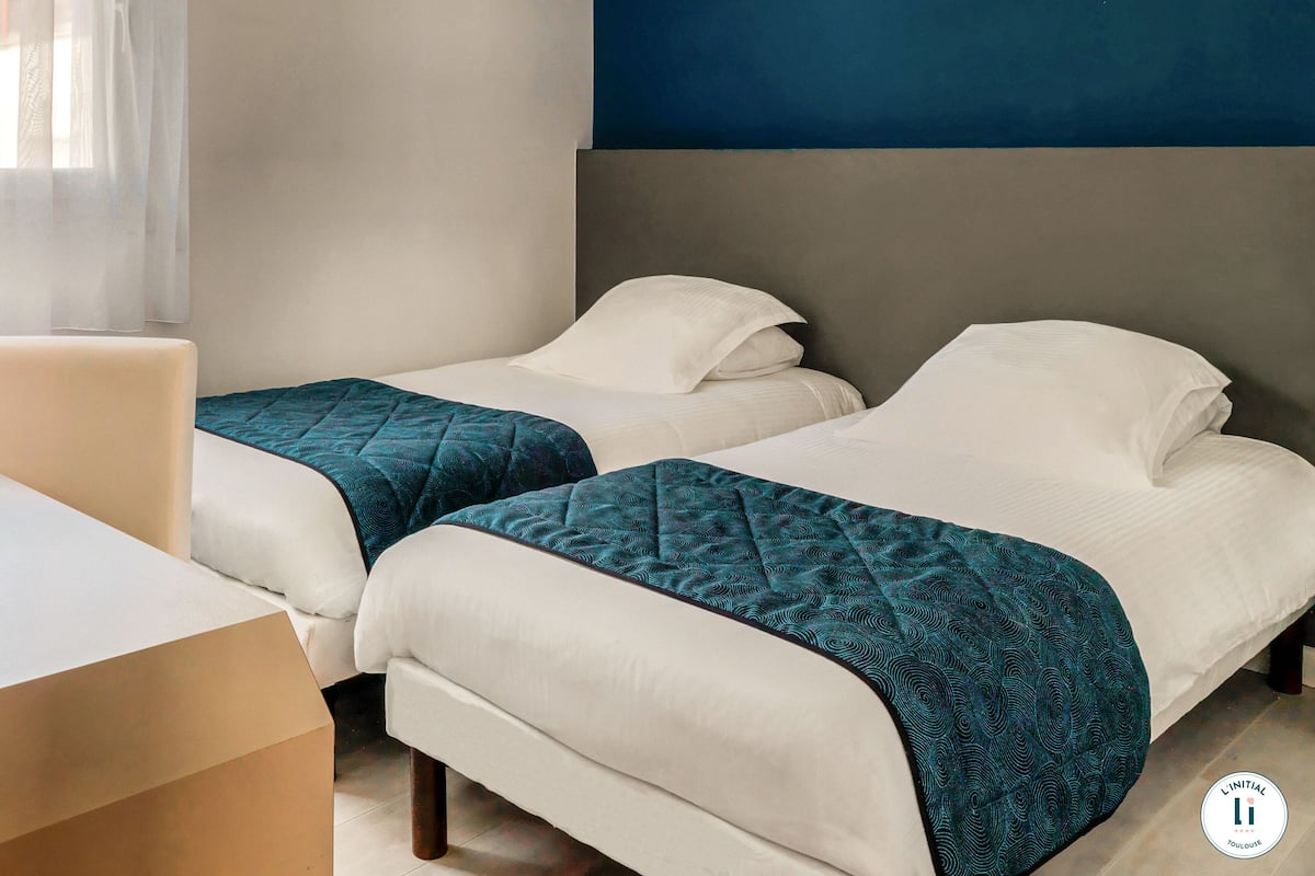 Habitación de hotel con dos camas, un escritorio y una ventana con cortinas traslúcidas.