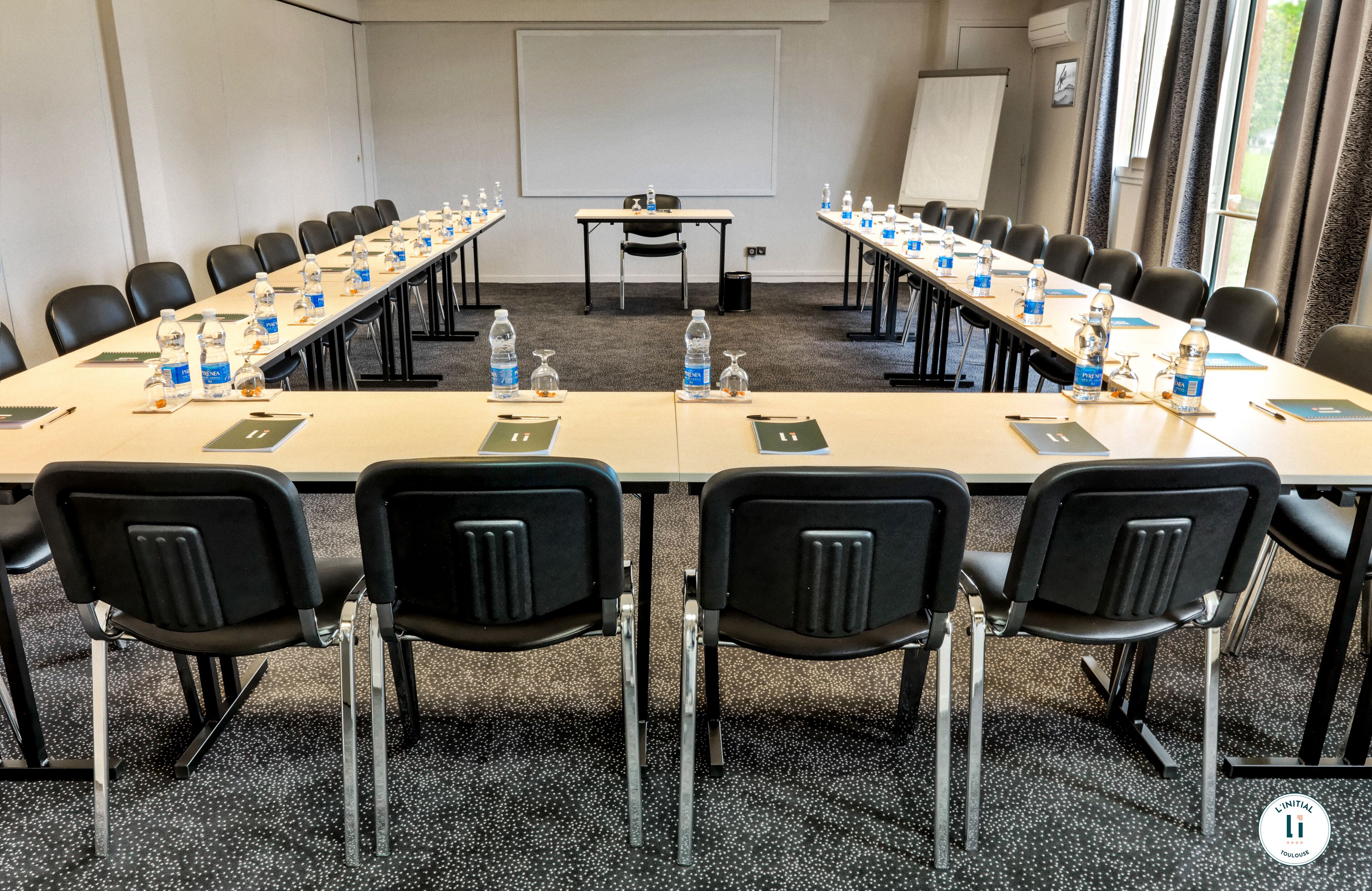 Un salón de conferencias con una larga mesa, sillas, botellas de agua, tarjetas de identificación y una pantalla de proyector.