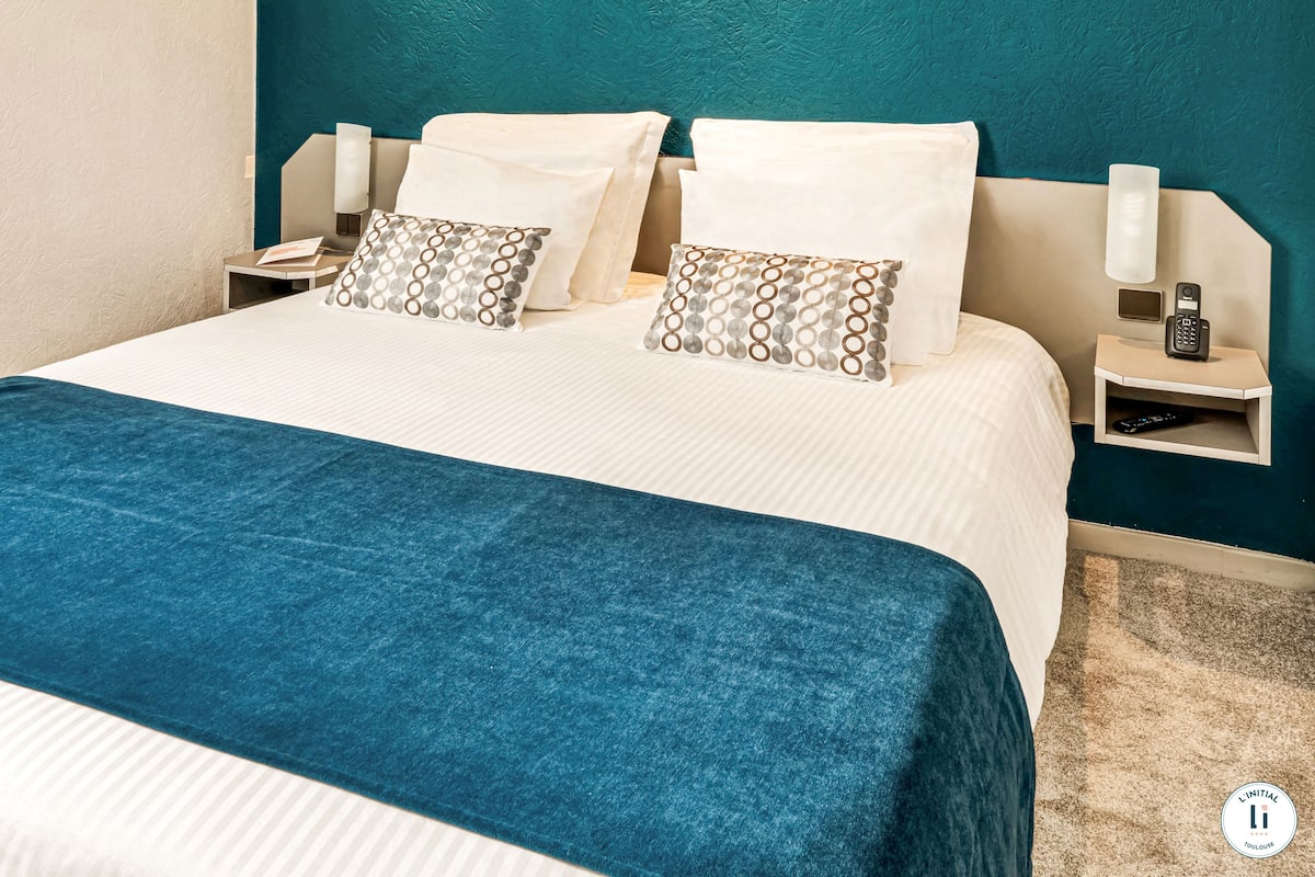 Una cama bien hecha con una colcha azul, almohadas blancas y una pared de acento color aguamarina.