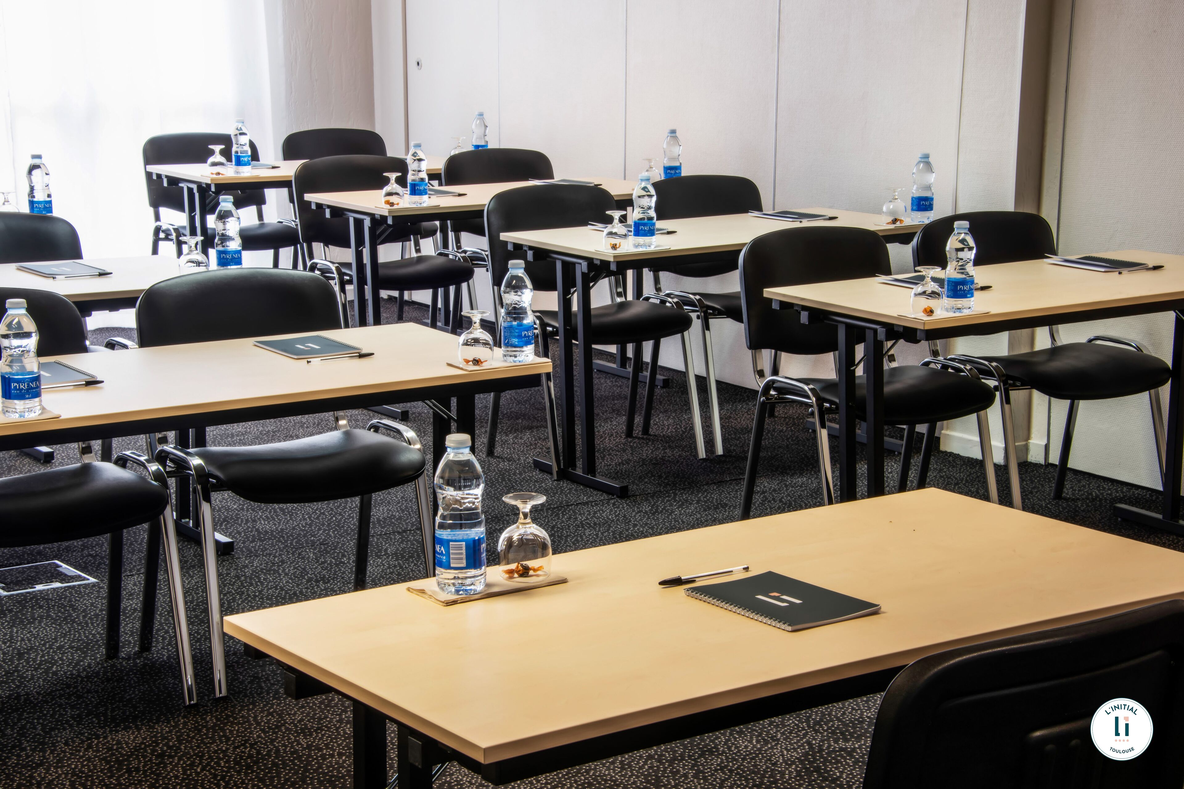 A conference room with multiple tables, chairs, water bottles, and a notebook.