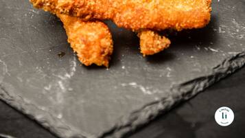 A slate serving board with breaded chicken tenders, a bowl of fruit, and a bowl of dip.