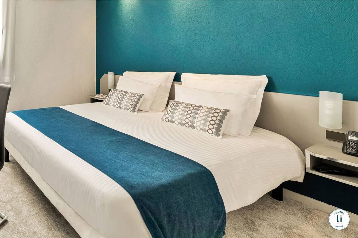 Habitación de hotel con cama, escritorio, silla y una pared de acento color aguamarina.