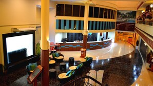 A lobby with a curved reception desk, seating area with round tables and chairs, and a large flat-screen TV. - De Rhu Beach Resort (Kuantan)