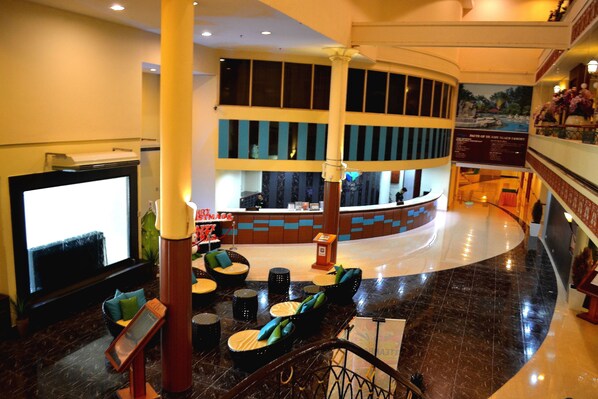 A lobby with a curved reception desk, seating area with round tables and chairs, and a large flat-screen TV.