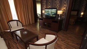 A hotel room with a wooden floor, a television on a cabinet, a chair, a table, and a lamp. - De Rhu Beach Resort (Kuantan)