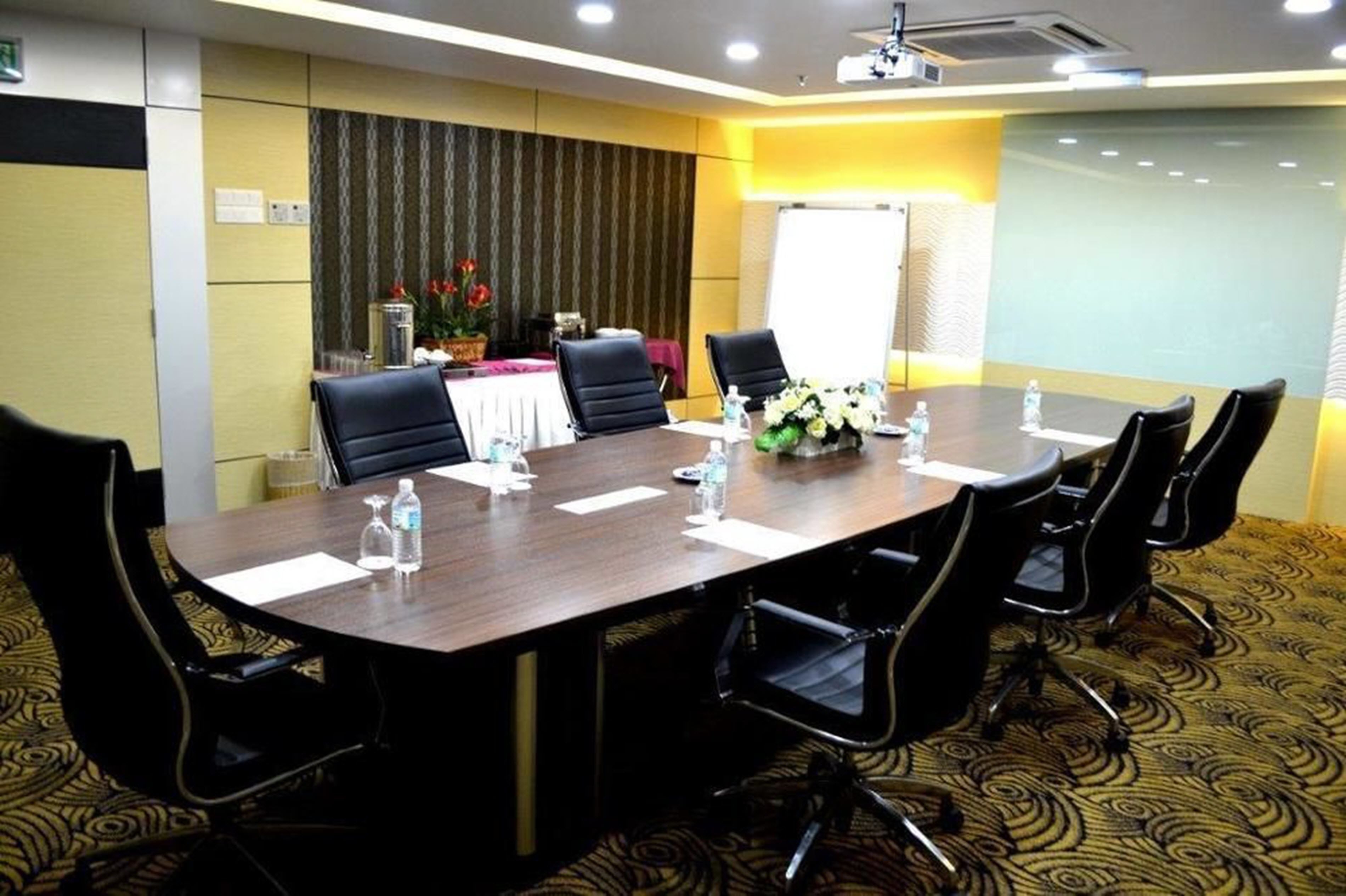 Une salle de conférence avec une longue table, des chaises noires, des bouteilles d’eau et un arrangement floral.