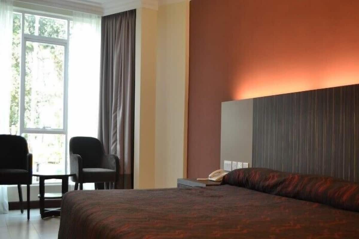 A hotel room with a large bed, a desk, two chairs, and a window with curtains.