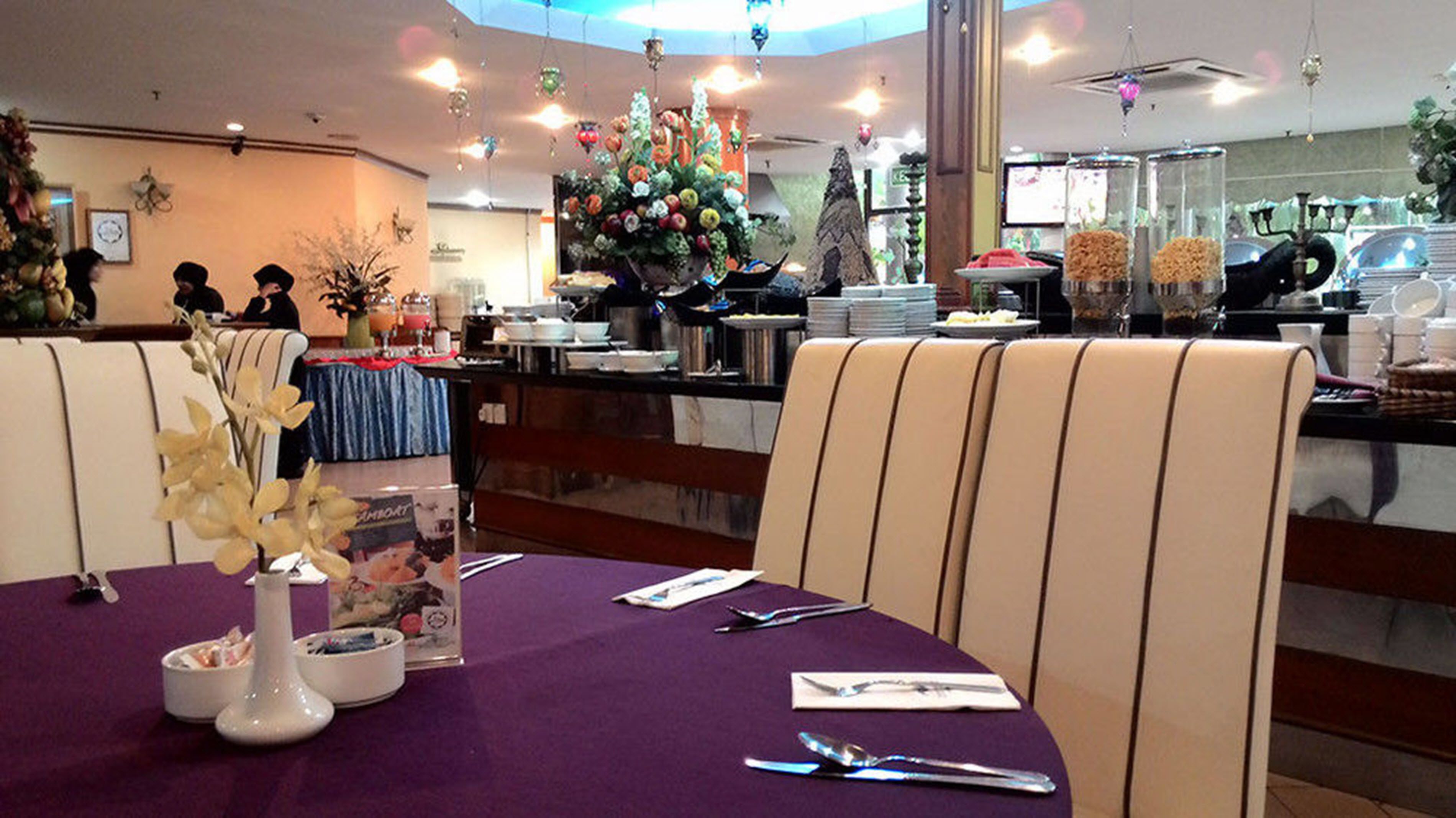 L’intérieur d’un restaurant, avec des nappes violettes, des chaises blanches et un buffet situé au fond de la salle.
