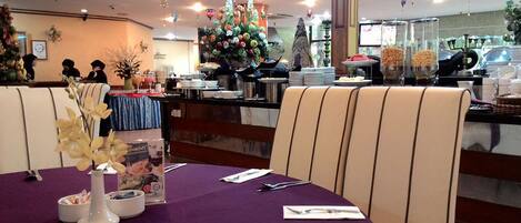 L’intérieur d’un restaurant, avec des nappes violettes, des chaises blanches et un buffet situé au fond de la salle.