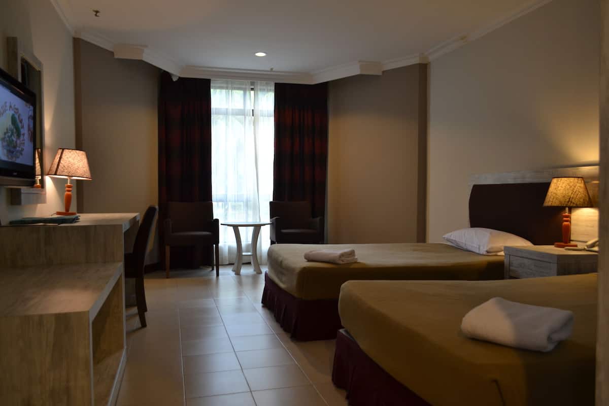 A hotel room with two beds, a desk, a chair, a TV, and a window with curtains.