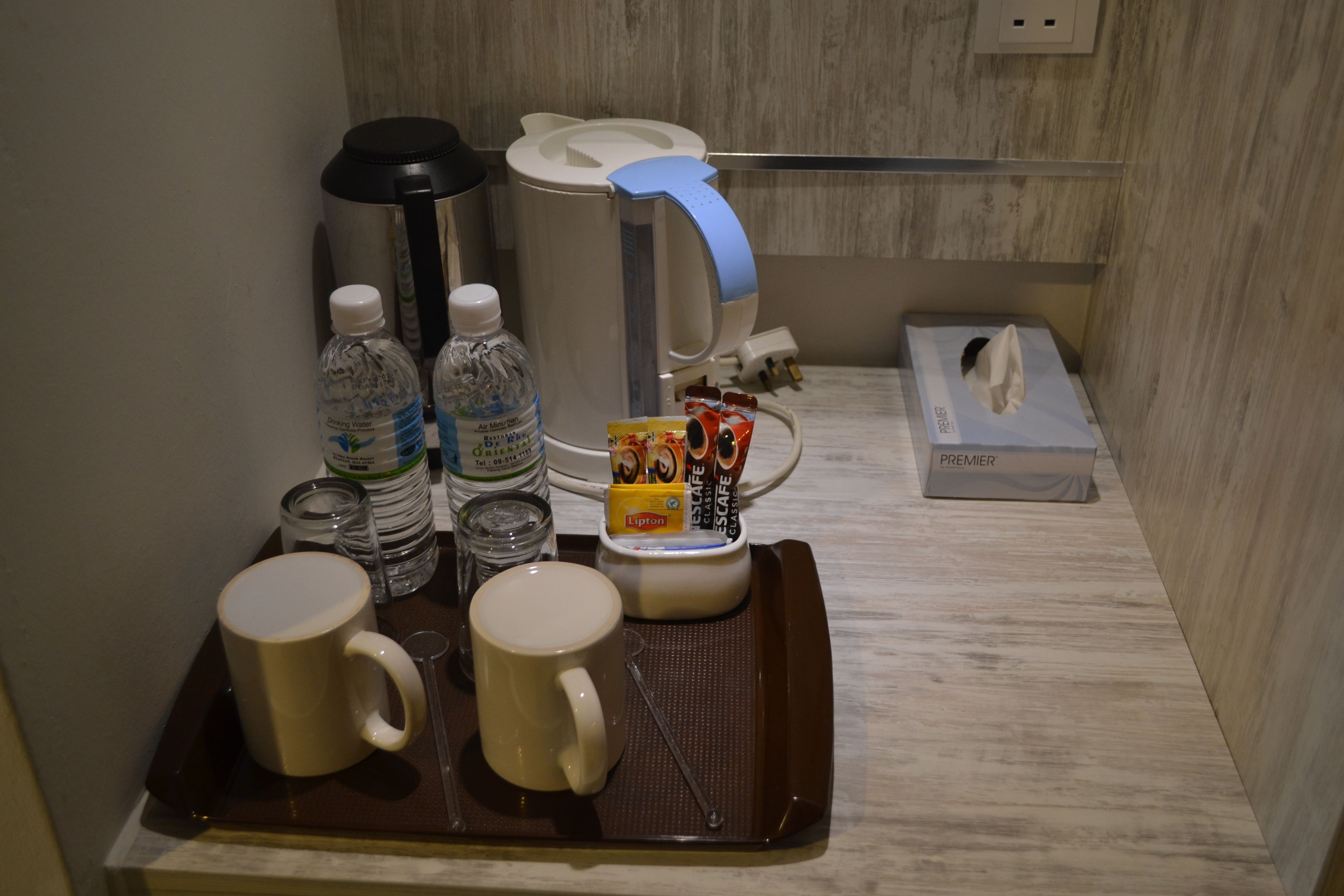 Hotelkamer met koffiehoek, inclusief koffiezetapparaat, waterflesjes en een dienblad met twee mokken.