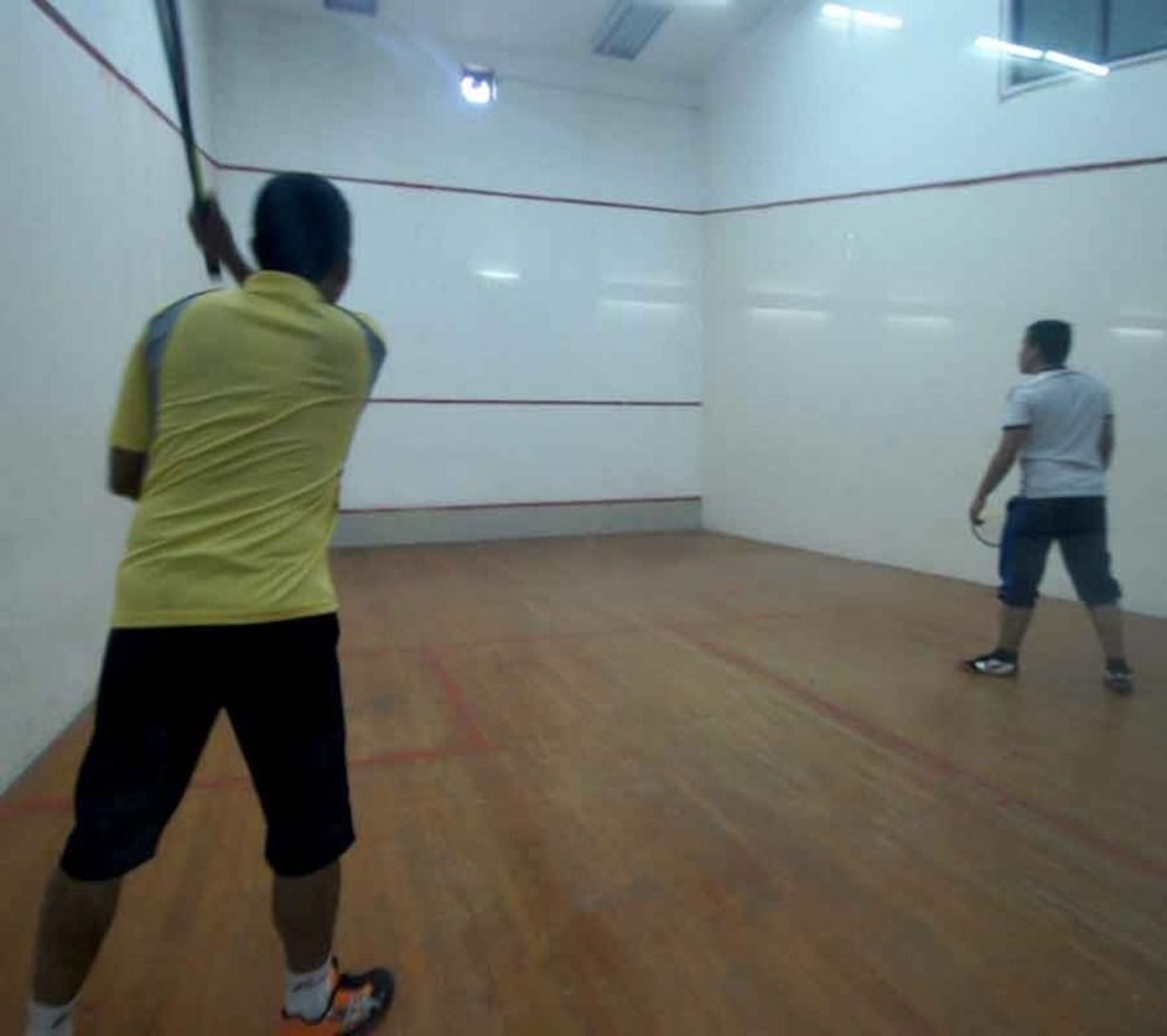 Una cancha de squash con piso de madera y paredes blancas.