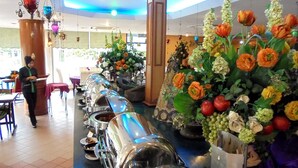 A buffet setup with multiple serving stations and a variety of flowers in the background. - De Rhu Beach Resort (Kuantan)