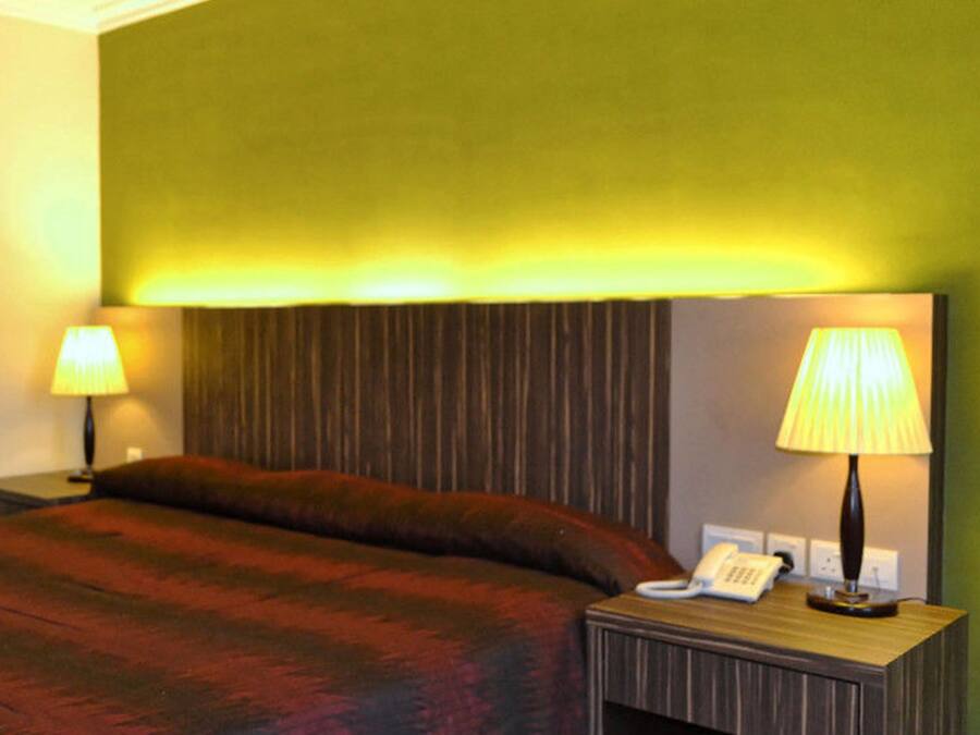 A hotel room with a bed, two bedside lamps, a telephone, and a wall with vertical paneling.
