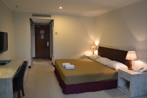 A hotel room with a bed, bedside lamps, a desk, and a television.