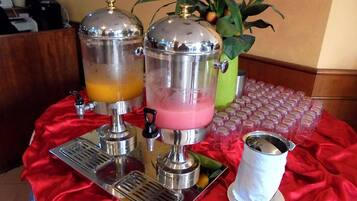 A beverage station with two dispensers, one with a yellow drink and another with a pink drink, and a tray with a metal cup.