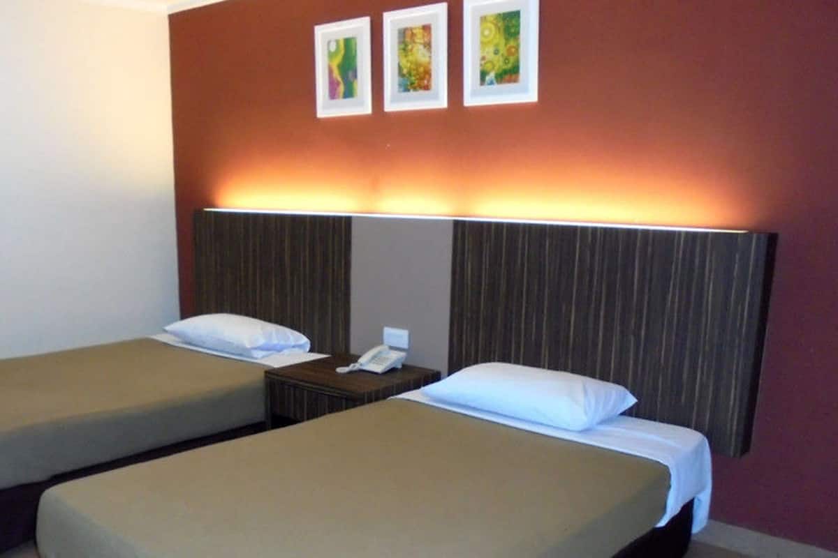 A hotel room with two single beds, a bedside table with a phone, and a wall with three framed pictures.