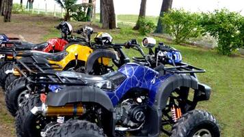A row of quad bikes parked on grass with trees in the background.