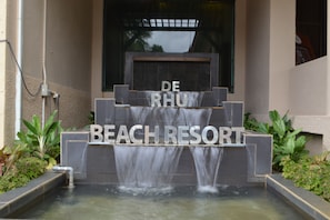 A water feature with the words "DE RHU BEACH RESORT" in front of a building entrance.