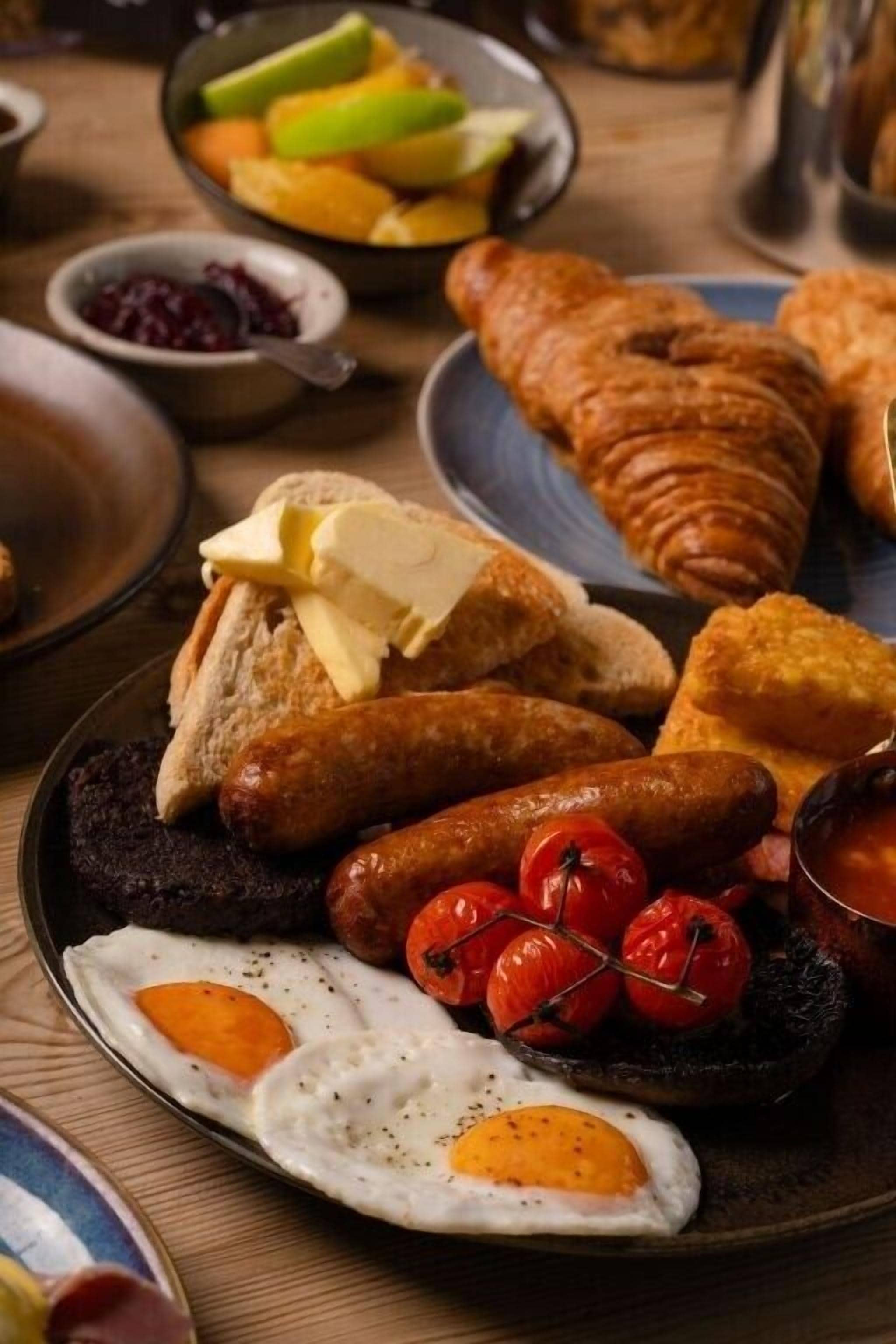 Une assiette de petit-déjeuner avec des œufs, des saucisses, des tomates et du pain.