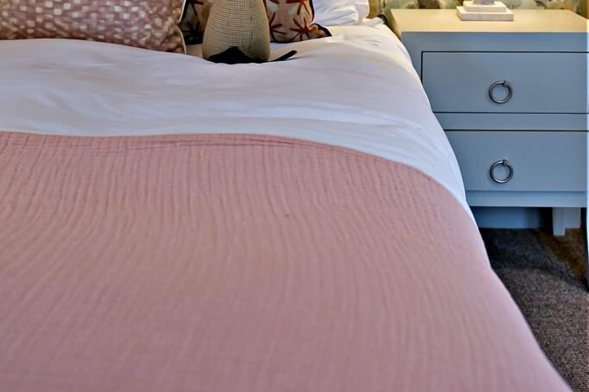 A bedroom with a tufted headboard, patterned pillows, a white bedspread, and a bedside lamp on a nightstand.