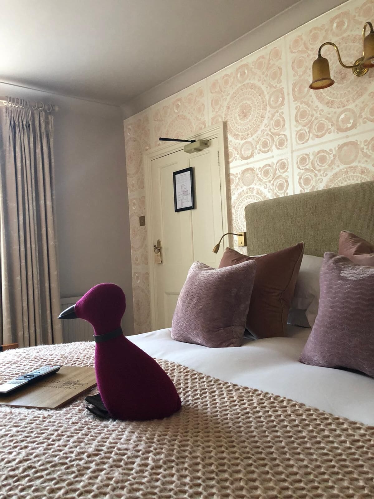 A hotel room with a bed, pillows, a plush toy, and a door with a framed picture.