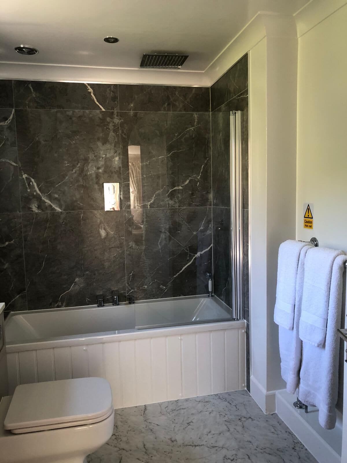 Un baño moderno con pared de mármol, una bañera independiente y un inodoro.
