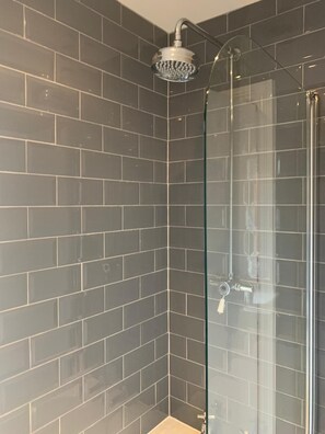 Ducha con mampara de vidrio, cabezal de ducha de mano, paredes de azulejos y panel de control a la vista.