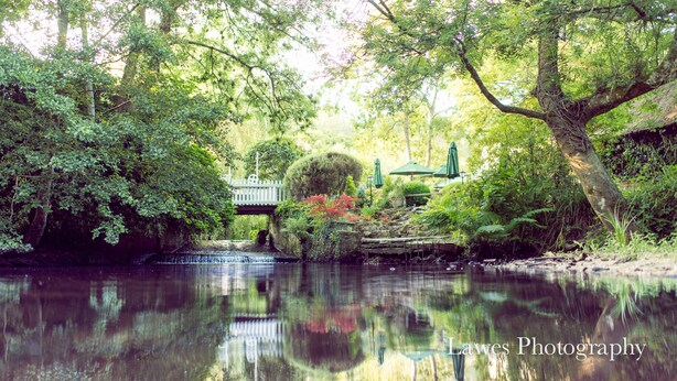 A serene riverside scene with a bridge, lush greenery, and a calm water body. - The Old Mill (Lymington)