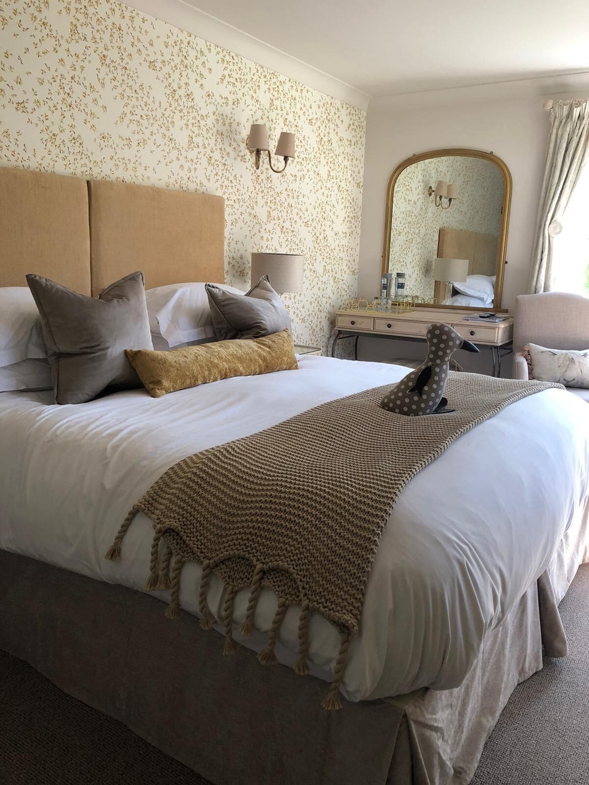 A neatly arranged hotel room with a large bed, a bedside table, a mirror, and a window with curtains.