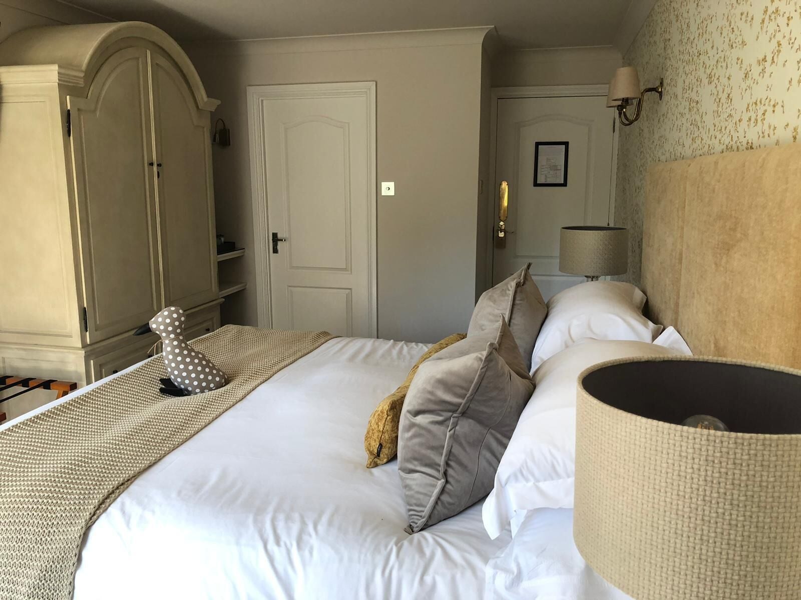 A neatly arranged hotel room with a large bed, a wardrobe, a lamp, and a wall-mounted light fixture.