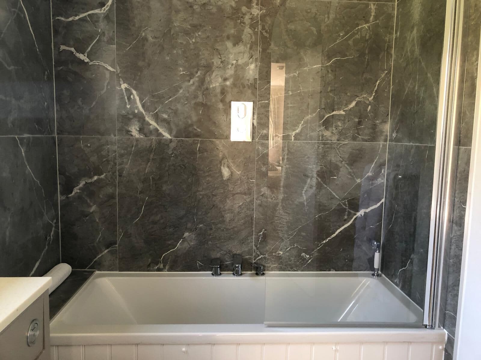 A bathroom with a bathtub, dark marble walls, and a white tiled floor.