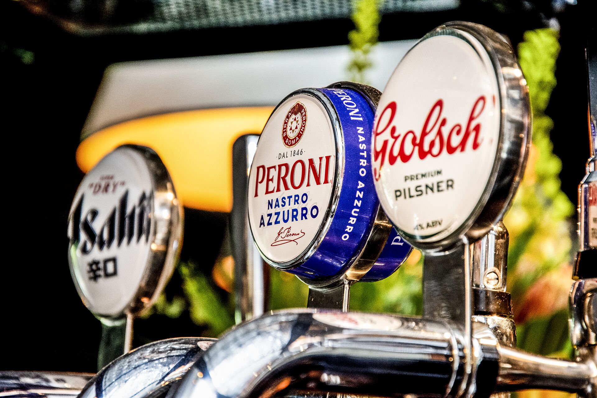 Gros plan sur des robinets à bière, dont les étiquettes indiquent « PERONI Nastro Azzurro » et « Grolsch Premium Pilsner ».