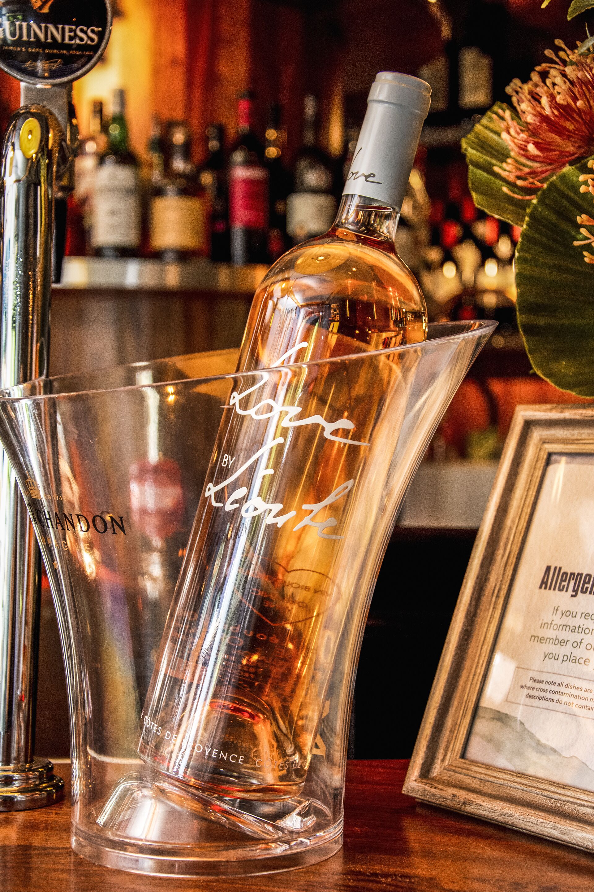 Un bar avec une bouteille de spiritueux, un pichet et un menu encadré.