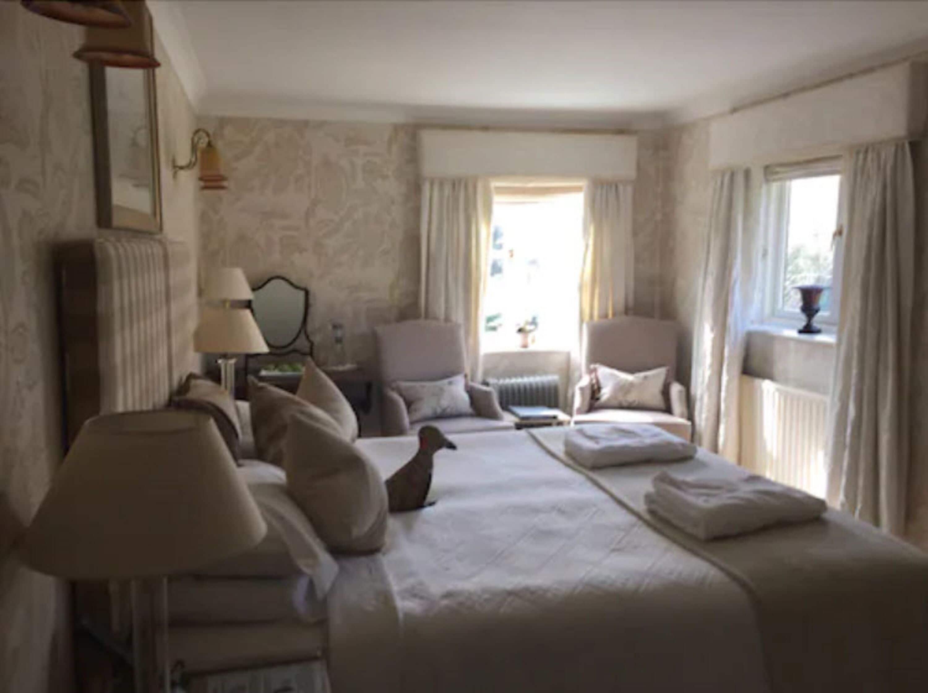 Una habitación de hotel con una cama grande, dos sillones, una mesita y un ventanal con cortinas.