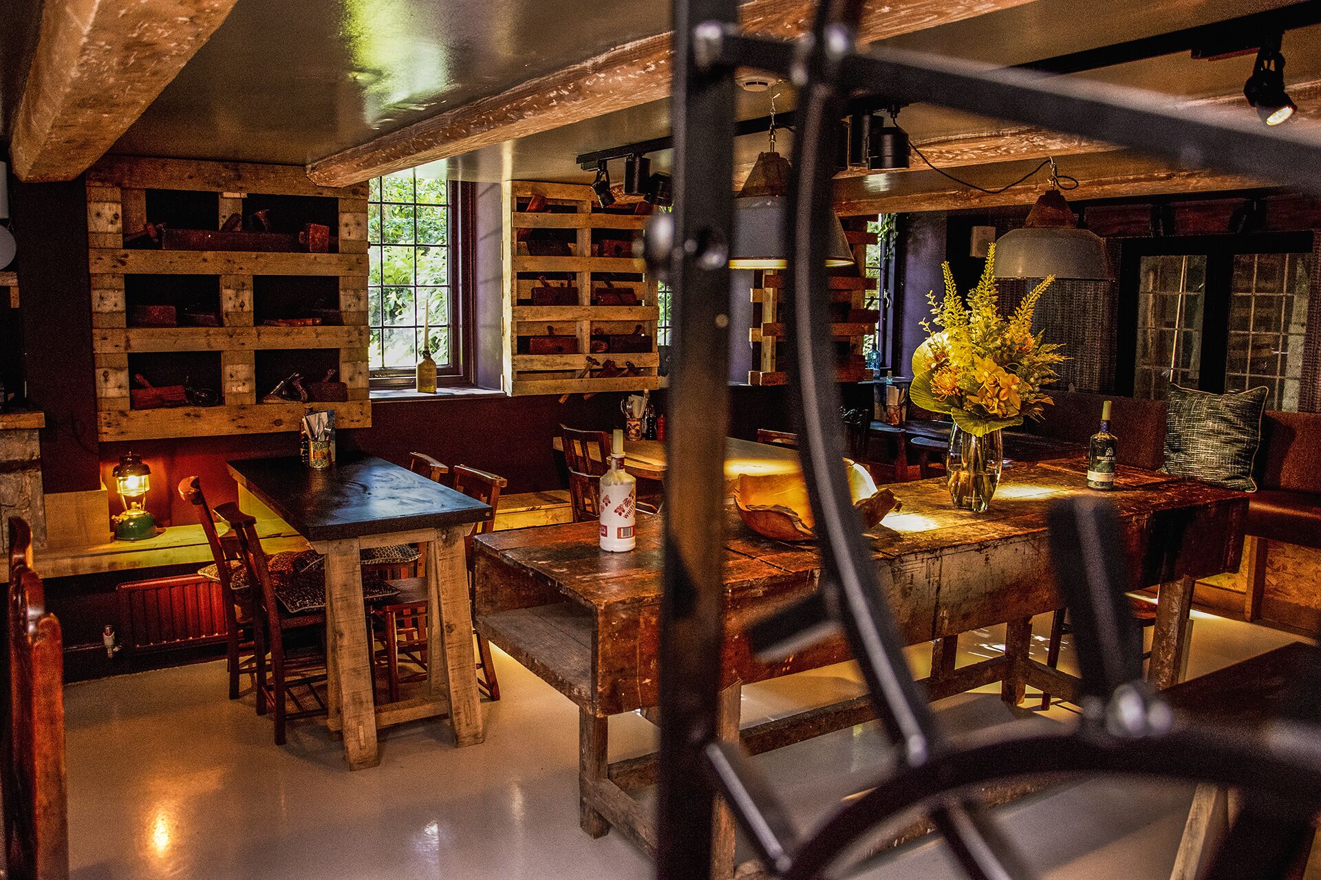 A rustic interior with wooden furniture, shelves with various items, and a large window allowing natural light.