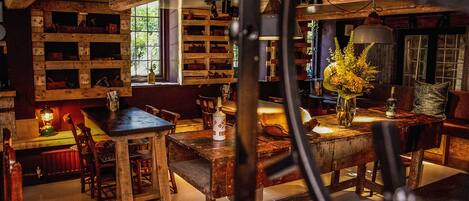 A rustic interior with wooden furniture, shelves with various items, and a large window allowing natural light.