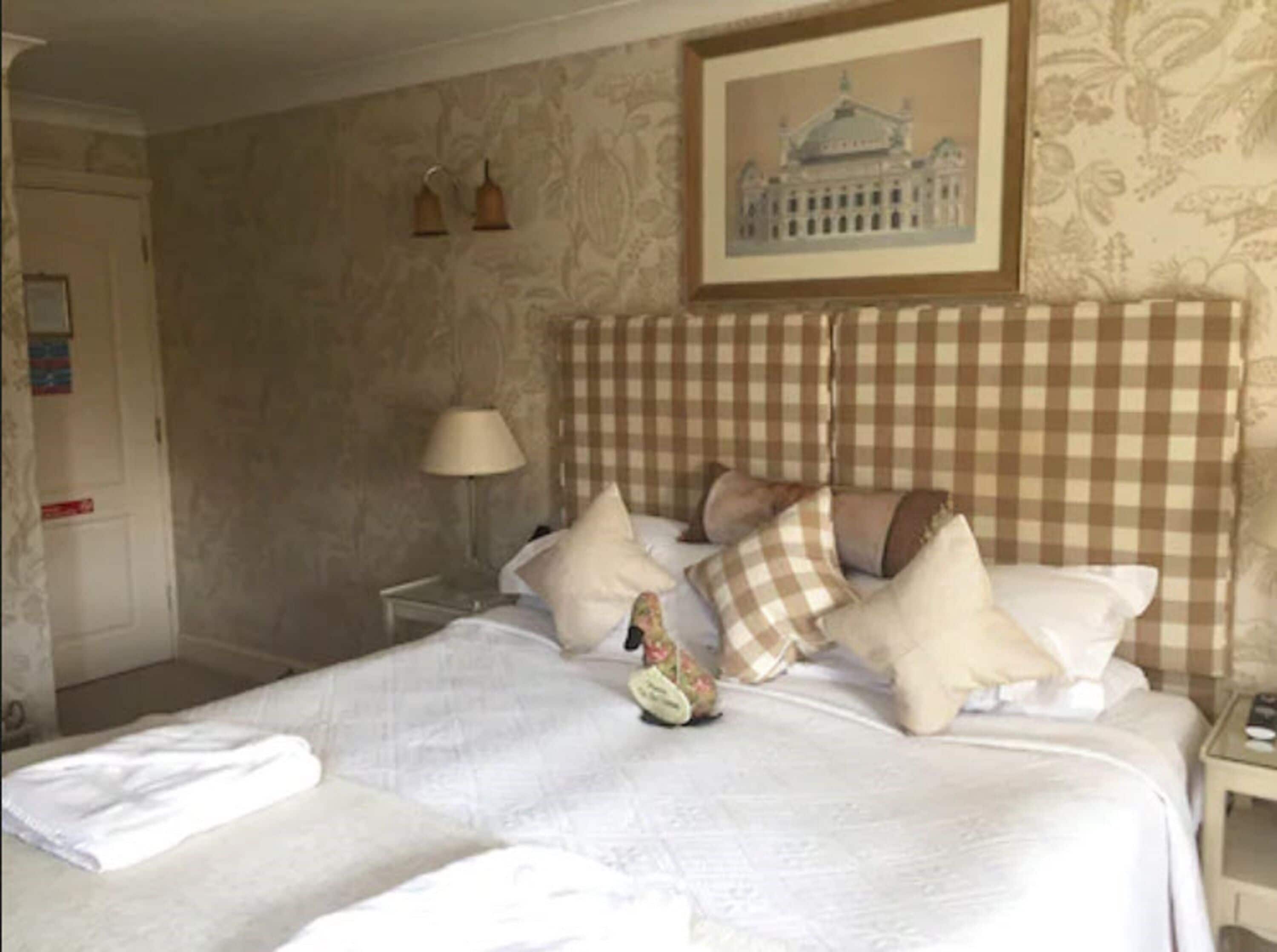 Una habitación de hotel con un cabecero a cuadros, una cama con varias almohadas, una mesita de noche con una lámpara y un cuadro enmarcado en la pared.