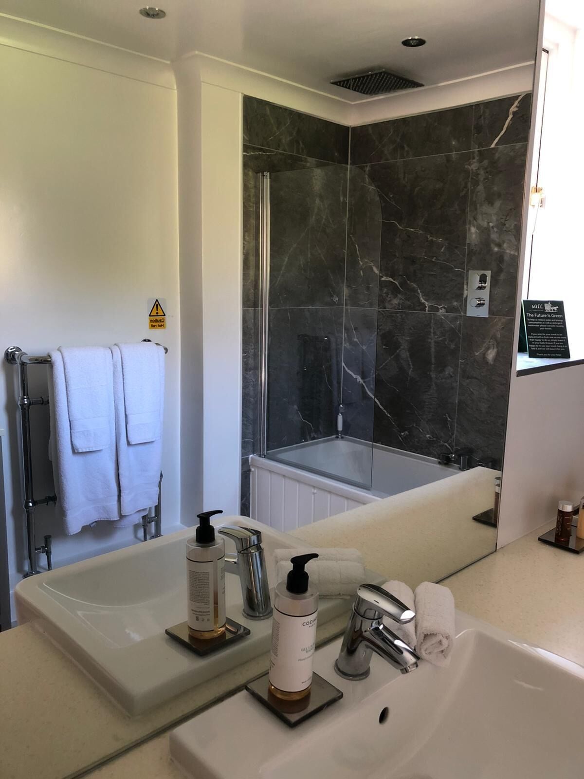 A modern bathroom with a large mirror, a bathtub, and a shower area with marble walls.