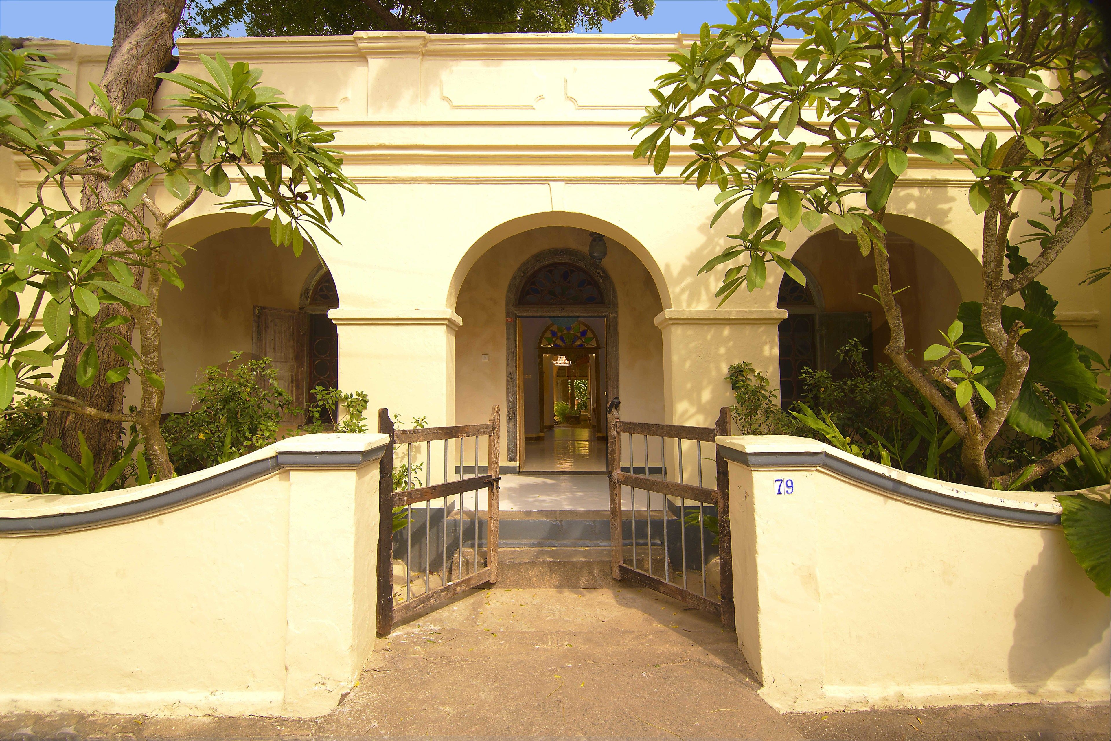 A building entrance with a gate, arched doorways, and surrounding greenery.